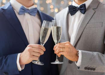 people, celebration, homosexuality, same-sex marriage and love concept - close up of happy married male gay couple drinking sparkling wine on wedding over holidays lights background