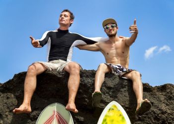 two friend surfer sitting on a rock showing sign ok