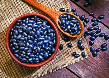 Top view of a brown bowl filled with black beans shot on rustic wood table. A wooden spoon is beside the bowl with some beans on it. DSRL studio photo taken with Canon EOS 5D Mk II and Canon EF 100mm f/2.8L Macro IS USM