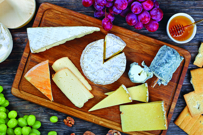 authentic french Cheeses served with grapes, honey and nuts on wooden background with triangle and round wooden containers made from poplar for packaging, view from above