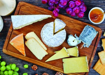 authentic french Cheeses served with grapes, honey and nuts on wooden background with triangle and round wooden containers made from poplar for packaging, view from above