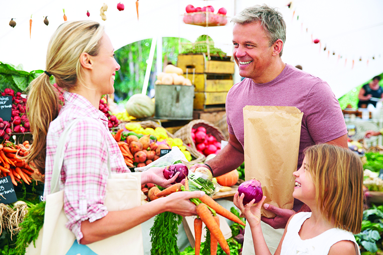 Family Buying Fresh Vegetables At Farmers Market Stall, Smiling