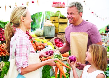 Family Buying Fresh Vegetables At Farmers Market Stall, Smiling