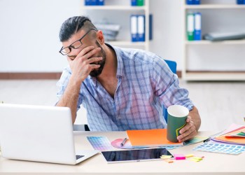 Upset interior designer sitting at his desk with a hand over his face