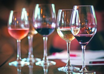 Closeup of five wineglasses arranged one next to the other, half full with several sorts of wines, red, white and rose wines. Glasses are on the table, there are some papers and pens in background as this was the detail from winetasting. Lit from both sides.