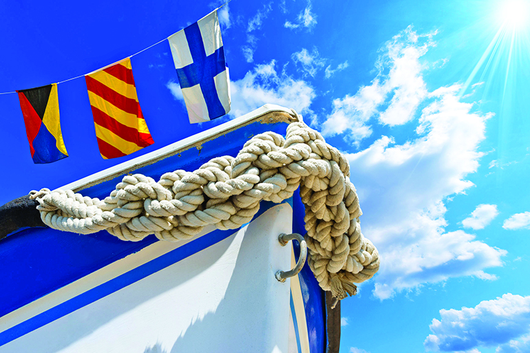 30574188 - bow of the boat adorned with knotted rope on blue sky with three nautical flags and space for text