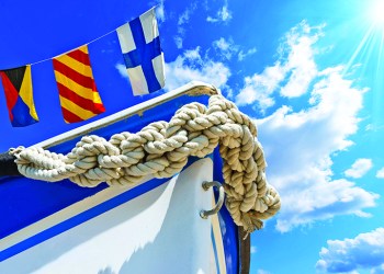 30574188 - bow of the boat adorned with knotted rope on blue sky with three nautical flags and space for text