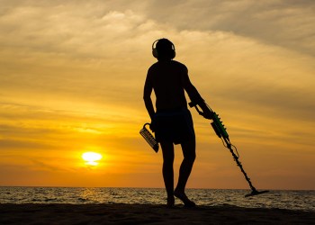 65484196 - a treasure hunter with metal detector on sunset on the beach