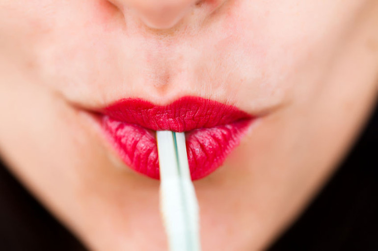 Woman wearing red lipstick using a straw