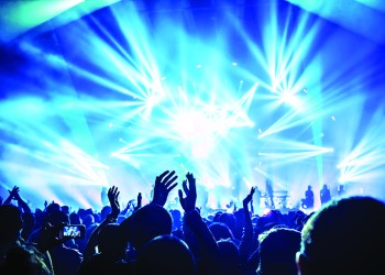 Large group of happy people enjoying rock concert, clapping with raised up hands, blue lights from the stage, new year celebration concept