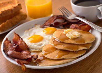 A delicous home style breakfast with crispy bacon, eggs, pancakes, toast, coffee, and orange juice.