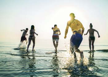 Group of happy friends running in to water at sunset - Silhouettes of active people having fun on the beach on vacation - Tourists going to swim on a tropical island