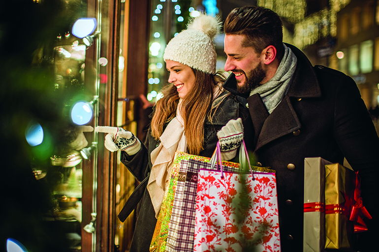 Young couple walking in downtown for Christmas. Holding Christmas gifts and big Teddy bear. Wearing warm clothing.