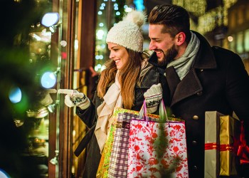 Young couple walking in downtown for Christmas. Holding Christmas gifts and big Teddy bear. Wearing warm clothing.