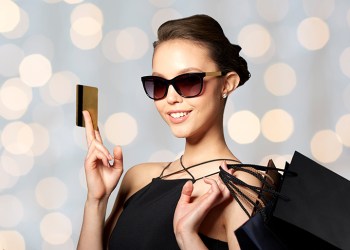 sale, finances, fashion, people and luxury concept - happy beautiful young woman in black sunglasses with credit card and shopping bags over holidays lights background happy woman with credit card and shopping bags