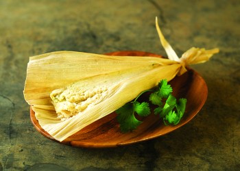 Mexican chicken tamale in corn husk on wood plate garnished with cilantro.