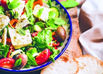 Traditional Greek salad with feta cheese, olive oil and olives and glass of red wine over rustic wooden serving board on white marble table, selective focus. Mediterranean local cuisine