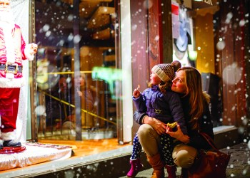 little toddler girl with mother on christmas market. funny happy kid making window shopping with santa claus. holidays, christmas, childhood and people concept. family during winter snowfall