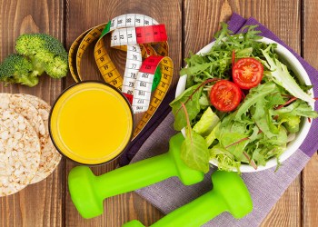 Dumbells, tape measure and healthy food over wooden table. Fitness and health