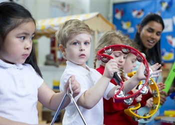 Nursery children playing with musical instruments in the classroom. One little boy is looking at the camera with a tambourine.