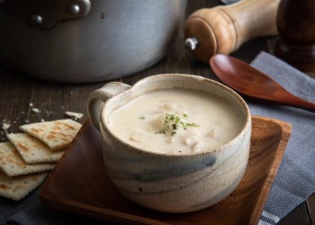 New England clam chowder in cermamic bowl with pepper grinder, pot and wooden spoon