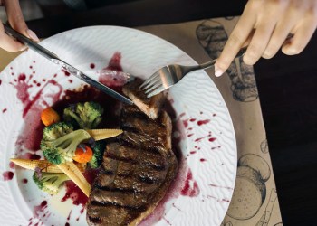 Female hands cutting road kill steak on plate with vegetables and red wine a jus splatter