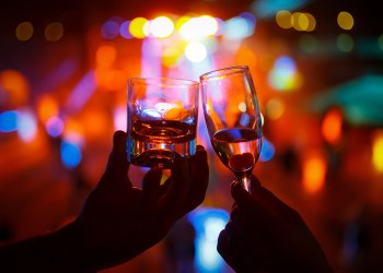 Wineglass of champagne in woman hand and a glass of whiskey in a man hand against a background of colored lights