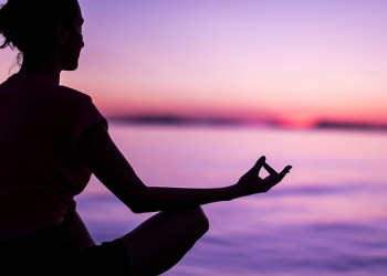 Calm Mindful Woman Meditating On Beach Faced Towards Majestic Sunset