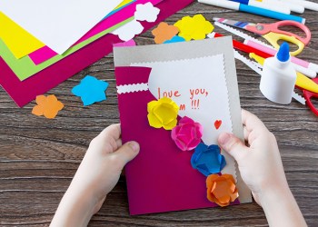 A child is holding a greeting card with flowers on Mother's Day. Children's art project, craft for children. Handmade. Craft for children. Valentine's Day