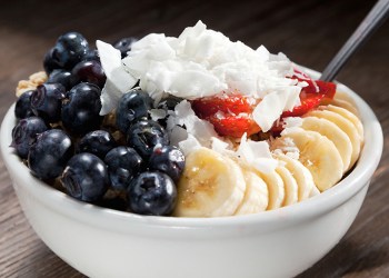 Blueberries, bananas, and coconut on top of acai served in a white bowl.