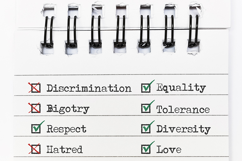 Spiral notebook page with green checks on the words Equality, Tolerance, Diversity, Love and Respect, and red Xs on Discrimination, Bigotry and Hatred