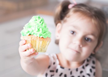 Cute little girl holding birthday cupcakes in kitchen. Festive and holiday concept