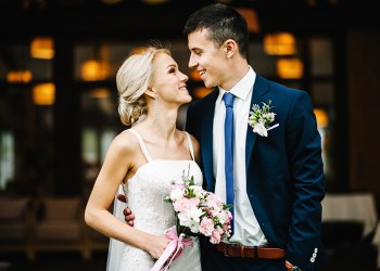 Romantic couple newlyweds, bride and groom holding bouquet of pink and purple flowers and greens with ribbon at the wedding ceremony. Happy and joyful wedding moment.