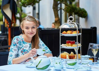 Beautiful young woman enjoying afternoon tea with selection of fancy cakes and sandwiches in a luxury Parisian restaurant