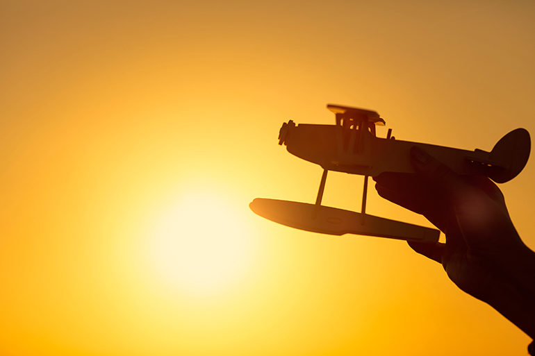 Hand holding toy airplane with sun behind it