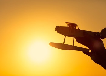 Hand holding toy airplane with sun behind it