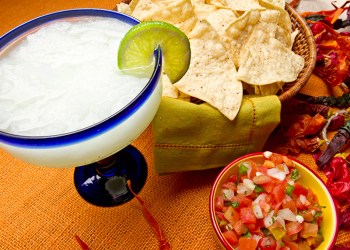 Margarita, chips and salsa on an orange backgroud with chili peppers.