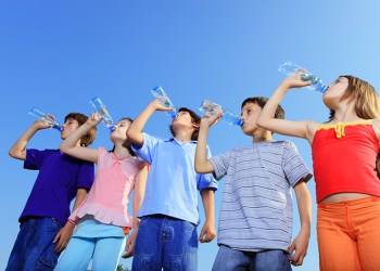 Children drinking water from bottles against the blue sky.