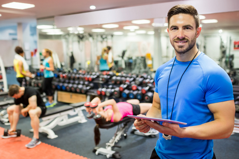 Handsome trainer using tablet in weights room at the gym