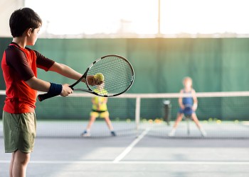 Cheerful kids playing tennis on court