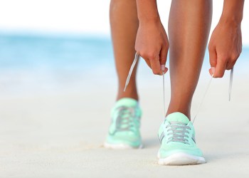 runner woman tying laces of running shoes preparing for beach jogging. closeup of hands lacing cross training sneakers trainers for cardio workout. female athlete living a fit and active life.