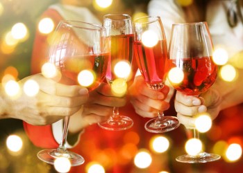 Hands holding wine glasses toasting the holidays with Christmas lights flickering