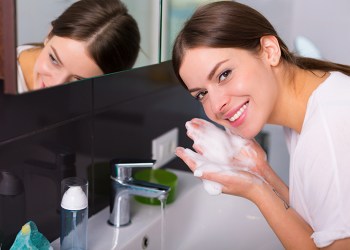 Woman washing up her face with foam cleanser in the morning