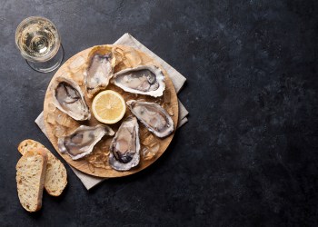 Opened oysters, ice and lemon on board and white wine on stone table. Top view with copy space