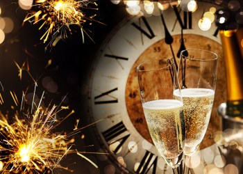 Festive New Years background with sparklers and champagne in front of a clock counting down to midnight with sparkling bokeh on darkness