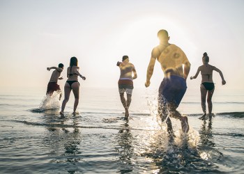 Group of happy friends running in to water at sunset - Silhouettes of active people having fun on the beach on vacation - Tourists going to swim on a tropical island