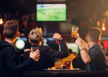 three men watches football on tv in a sport bar