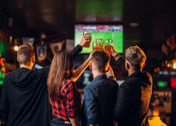 Fun friends watches football on TV and raised their glasses with beer in a sport bar, happy fans, celebration of the victory in game