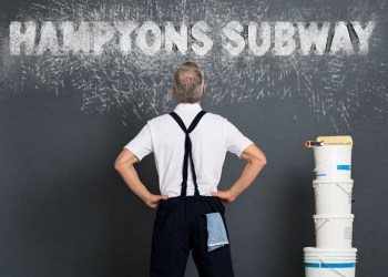 Rear view of painter looking at grey wall to paint. Mature workman with paint bucket and roller looking up at expressively painted Hamptons Subway sign