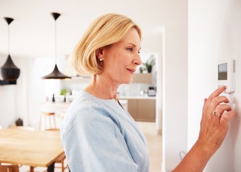 Close Up Of Mature Woman Adjusting Central Heating Temperature At Home On Thermostat